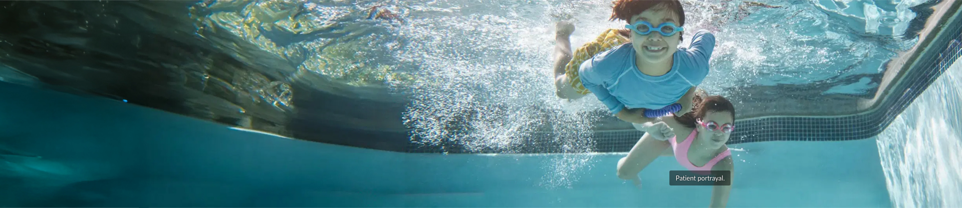 A young boy and young girl swimming underwater in a pool