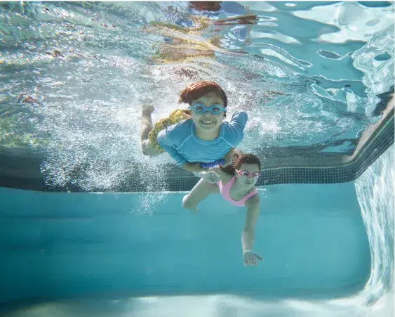 A young boy and young girl swimming underwater in a pool
