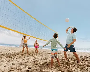 Family of 4 playing volleyball at the beach