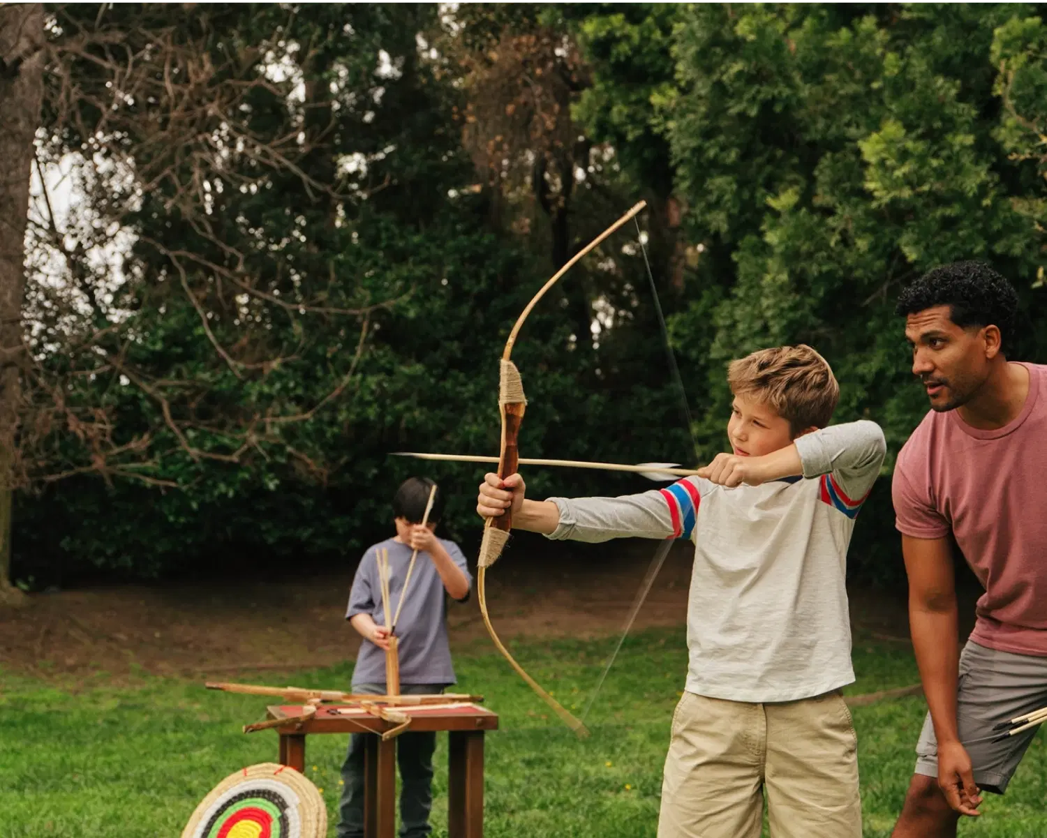 Child using a bow and arrow with an adult supervising