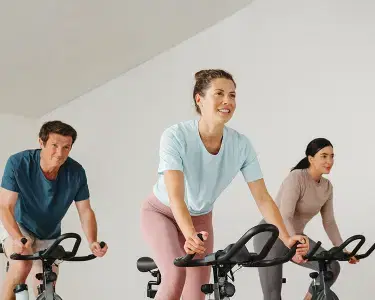 3 people (two women and a man) at the gym doing a spin class on indoor bicycles