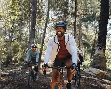 Three males cycling throughout a forest chatting and smiling as friends.