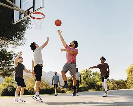 People playing basketball in a park on a sunny day