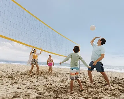 Family of four playing volleyball at the beach on a blue sky day